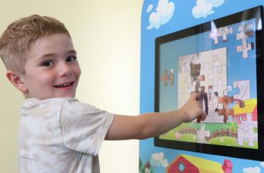 Ein Kind tippt auf einen Bildschirm. Auf dem Bildschirm läuft ein Puzzle-Spiel.